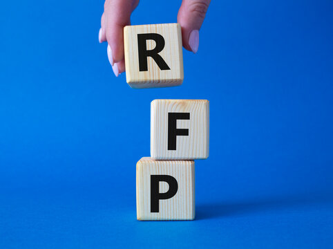 RFP - Request for Proposal. Wooden cubes with word RFP. Businessman hand. Beautiful blue background. Business and Request for Proposal concept. Copy space.