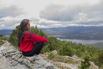 Naklejka premium lonely woman sitting on a mountain looking at the landscape and a lake