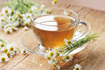 Chamomile herbal tea in a glass cup with flowers on wooden rustic background, closeup, winter cold...