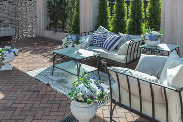 a chic terrace of a country house with wrought iron furniture, vases with flowers and columns on a bright summer sunny day