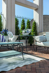 a chic terrace of a country house with wrought iron furniture, vases with flowers and columns on a bright summer sunny day