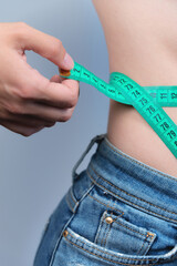 Waist of a slim woman in jeans. Close-up of a slim woman measuring the size of her waist with a tape measure