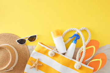 Sunscreen products for sun safety idea. Top view flat lay of UV-protection mockups, handbag, eyewear, footwear, hat, starfish, sand on yellow background with empty space for promo or message