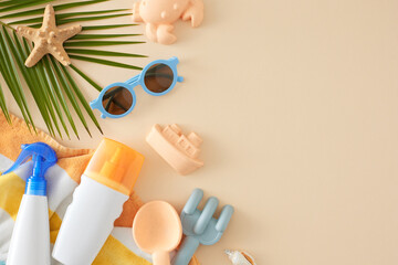 Children's summer skin care concept. Top view photo of UV-protection sprays, sunglasses, beach toys, palm leaf, seashell, starfish, beach towel on pastel beige background with space for advert or text