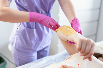 A beautician makes a sugar paste depilation of a woman's hand in a beauty salon. Female cosmetology. Removing unnecessary hair on the hand.  Sugar depilation. Depilatory sugar paste