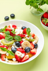 Summer fruit and berry salad with feta cheese, fresh strawberries, blueberries, banana, kiwi, orange and mint, green background, top view