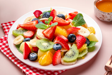 Summer fruit and berry salad with fresh strawberries, blueberries, banana, kiwi, orange and mint, pink background, top view