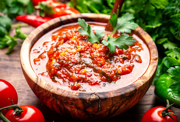 Traditional armenian spicy adjika sauce with hot pepper, paprika, tomatoes, garlic and parsley on rustic wooden kitchen table background, top view