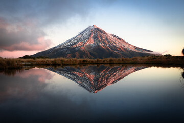 Mount Egmont, also called Mt Taranaki on the north Island of New Zealand during sunset with a beautiful reflection in the water of a little lake
