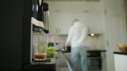 Process of making coffee in coffee machine. Blurred background of white kitchen furniture. Blurred silhouette of albino man talking on mobile phone. High quality 4k footage - Powered by Adobe