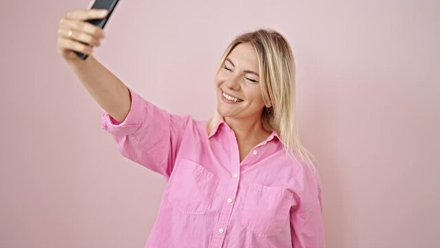 Young blonde woman smiling confident making selfie by the smartphone over isolated pink background