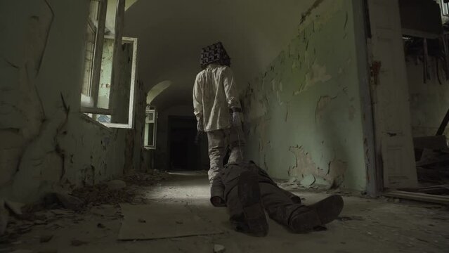 Ghost of maniac with cage on his head dragging dead body down corridor of asylum