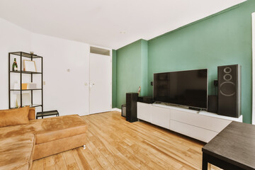 a living room with wood flooring and green walls, including a large flat screen tv set on the wall