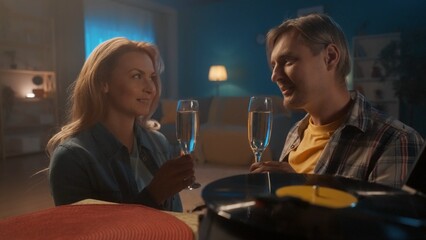 A young couple is sitting on the floor next to a vintage turntable close up. A married couple spends the evening with a glass of champagne, listening to pleasant music.