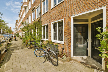 a bike parked on the side of a street in front of a brick building with white windows and plants growing next to it