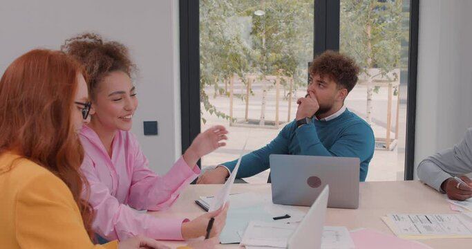 boring bearded pensive businessman piking his nose, he is fed up working in the office Tired man thinking about rest while his female colleagues are having fun laughing talking discussing project
