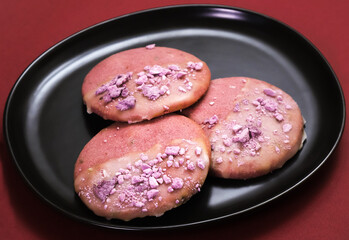 Pink cookies with lavender flavor in a black plate on a burgundy table. Close-up