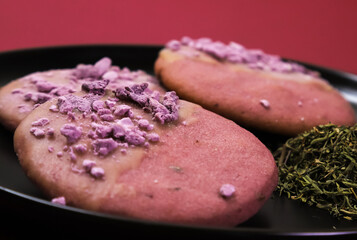 Pink cookies with lavender flavor in a black plate on a burgundy table. Close-up