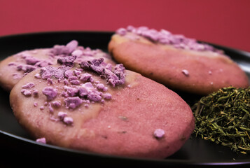Fototapeta na wymiar Pink cookies with lavender flavor in a black plate on a burgundy table. Close-up