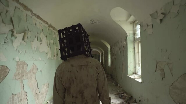 Ghost of maniac with cage on his head walking down corridor of abandoned asylum.
