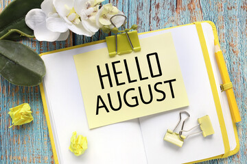 Hello August text on a yellow sticky note attached to a notepad near beautiful flowers