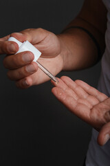 Brown skin tone man hands applying facial serum oil cosmetic product with white pipette dropper onto fingers. Studio environment and dramatic lighting.