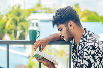 Young man reading book in the morning with a cup of coffee, morning routine. Healthy lifestyle of...