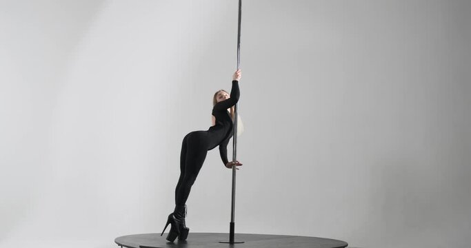Caucasian dancer captivates with seductive pole dance. Dressed in a sleek black dance bodysuit and high heels, she effortlessly moves around the pole, showcasing her grace, strength, and flexibility