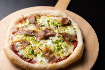 Close-up view of pizza with ham, zucchini, green pepper and mozzarela, on a wooden shovel