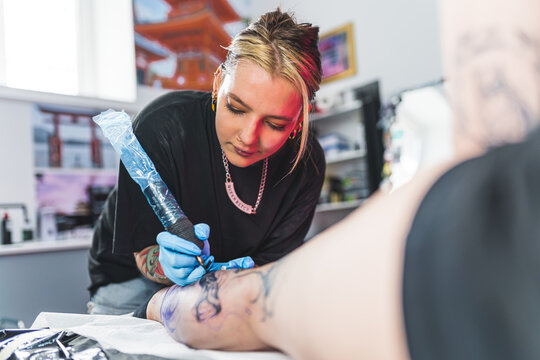 pretty tattoo master girl drawing on a customer's leg, medium shot tattoo art concept. High quality photo