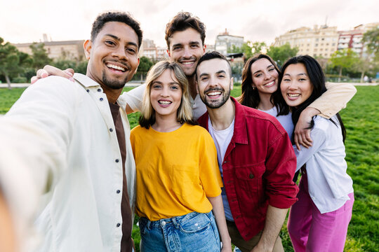 Young group of diverse college friends taking selfie standing together outdoors. Happy youth community of student people laughing and having fun together at campus university.