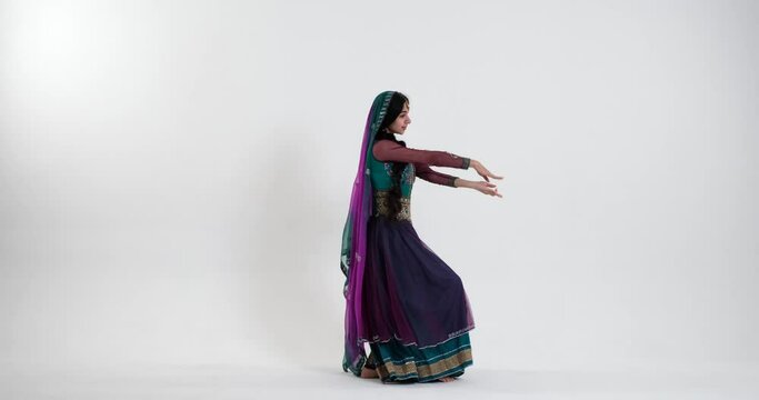 A young Indian woman dances on white background energetically to traditional music, dressed in a colorful sari with blue, purple, and green hues, and adorned with traditional Indian jewelry.