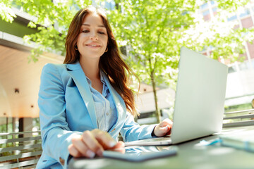 Portrait of smiling copywriter using laptop, taking mobile phone, sitting at workplace, remote job