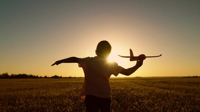 Child aviator, Boy wants to become pilot, astronaut. Slow motion. Happy kid runs with toy airplane on field in sunset light. Children play toy airplane. Teenager dreams of flying and becoming pilot.