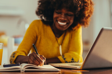 Close up of a happy casual businesswoman writing down tasks in agenda while working remotely from...