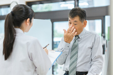 薬局で病気を説明する中高年男性と薬剤師・調剤師（服薬指導・鼻・鼻炎・花粉症）
