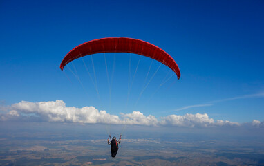 red Paraglider flying over valley on a clear day with blue sky