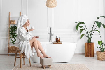 Beautiful young woman smelling body cream in bathroom, space for text