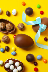 Tasty chocolate eggs and candies on yellow background, flat lay