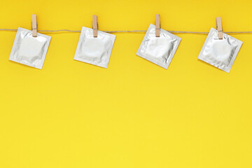 Clothesline with packaged condoms on yellow background, space for text. Safe sex