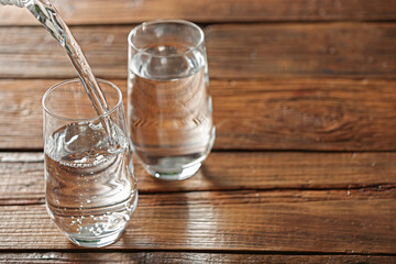 Pouring water into glass on wooden table, space for text