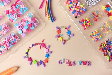 Fototapeta na wymiar Handmade jewelry kit for kids. Colorful beads, wristbands and bracelets on beige background, flat lay