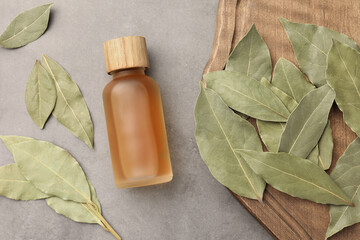 Bottle of bay essential oil and dried leaves on light grey table, flat lay