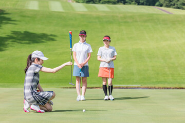 Obraz premium ゴルフ場のグリーンでゴルフをするゴルファーの女性(パター) 
