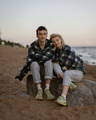 Young couple sitting on a rock in the evening covered with blankets from the cool wind