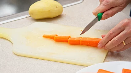 Fotobehang Hand held paring knife slicing carrot on cutting board © JohnBlottman