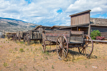 Fototapeta na wymiar Historic wagons and buildings with mountains, blue sky, and clouds. Wyoming, USA