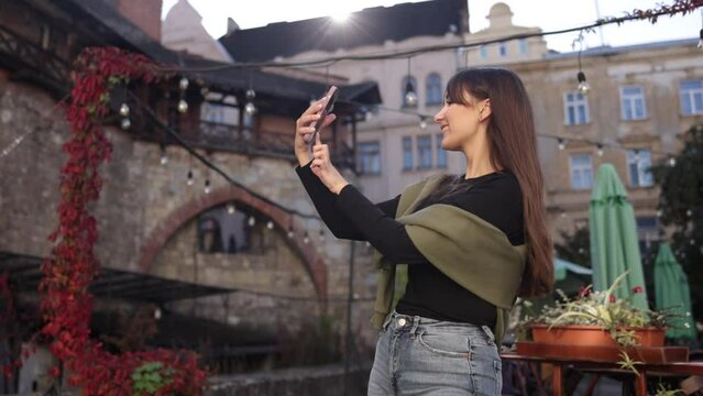Trendy snapshot, Urban background, Blogger photo. Captivating young lady snaps self-portrait using mobile device.