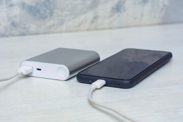 Smartphone charging with power bank on a gray wooden table. Portable charger for charging devices.