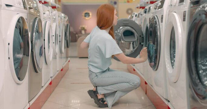 redhead girl opening the door odf washing machine, testing checking it at store Slow motion Black Friday, sale